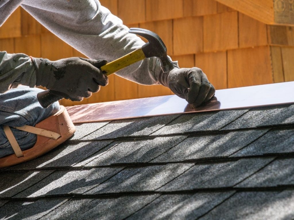 A professional roofer installing new siding and roofing shingles on a house roof
