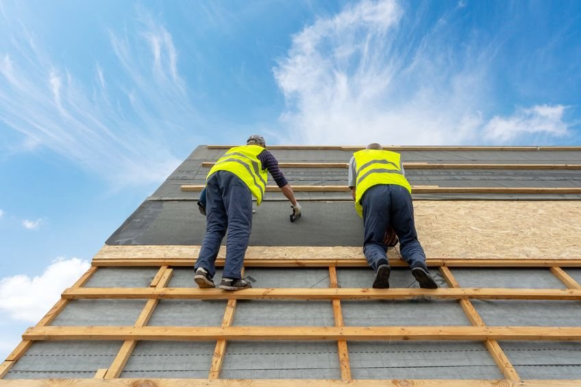 concept of renovation, repair and fixing frame work house. two professional workman in protective uniform wear standing on rooftop with special waterproof bitumen membrane on new building construction